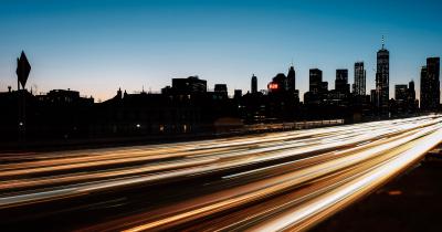 Blur of traffic light in front of backlit Manhattan skyline