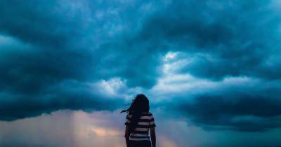 View of woman from behind as she looks out at incoming storm clouds
