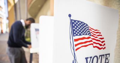 Black voter at a distance in a voting booth with an empty booth in the foreground