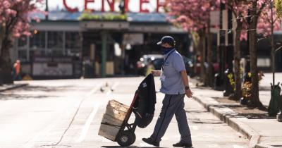 Masked postman pushing dolly on empty street