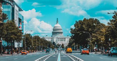 DC Capitol building at a distance in the day with cars in the foreground driving toward it 