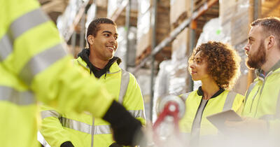 Diverse group of warehouse workers meeting among the warehouse shelves.