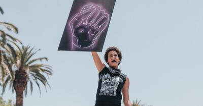 Black woman at a protest, holding up a sign of a neon black fist