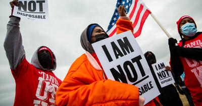 For Us Not Amazon action involving Black organizers dressed for cold weather, carrying 'I am not disposable' signs and carrying an American flag.