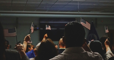 A depiction of a naturalization ceremony including a group of individuals waving flags