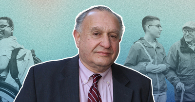 A man in a suit and tie stands in the foreground, smiling softly. In the background, a young man in a wheelchair and two people walking convey themes of support and inclusion.