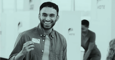 Man smiling holding an I Voted sticker at a polling station.