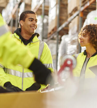 Diverse group of warehouse workers meeting among the warehouse shelves.