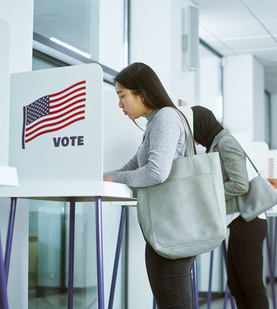 A group of multiracial voters voting at booths in a modern polling location, demonstrating civic participation and democratic engagement