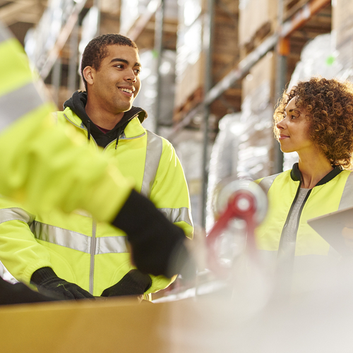 Diverse group of warehouse workers meeting among the warehouse shelves.