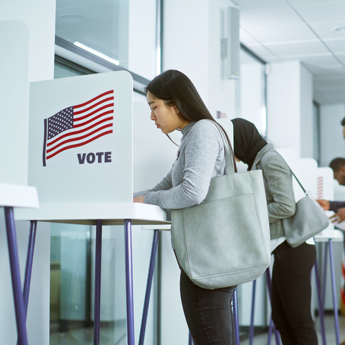 A group of multiracial voters voting at booths in a modern polling location, demonstrating civic participation and democratic engagement