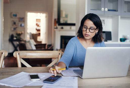 Woman at kitchen table with computer, calculator, and papers