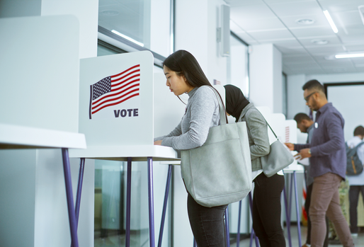 A group of multiracial voters voting at booths in a modern polling location, demonstrating civic participation and democratic engagement