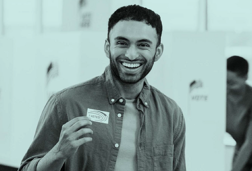 Man smiling holding an I Voted sticker at a polling station.