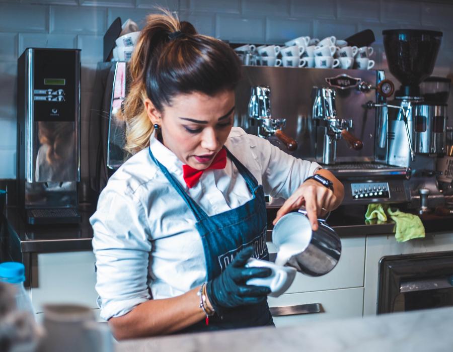 Latina barista pouring steamed milk into a latte in a coffee shop