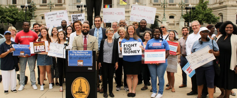 A multiracial group of people holding up sign in support of Fair Elections in Baltimore