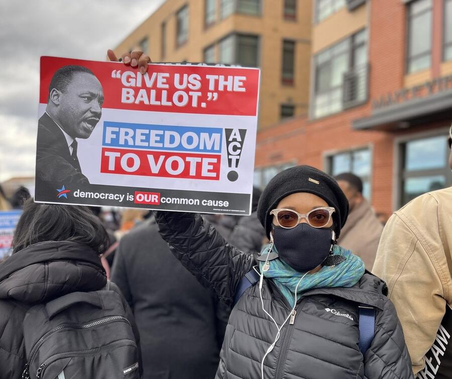 Taifa Smith Butler holding up a poser of MLK that reads "Give us the Ballot"